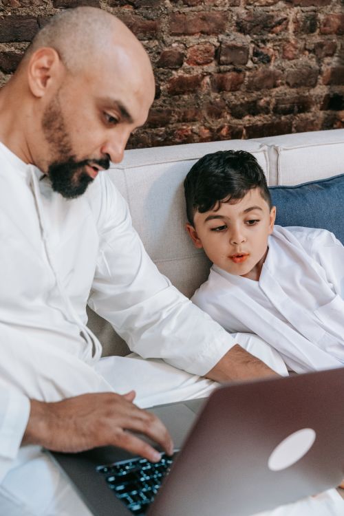 Free Father and son in traditional attire bonding while looking at a laptop at home. Stock Photo