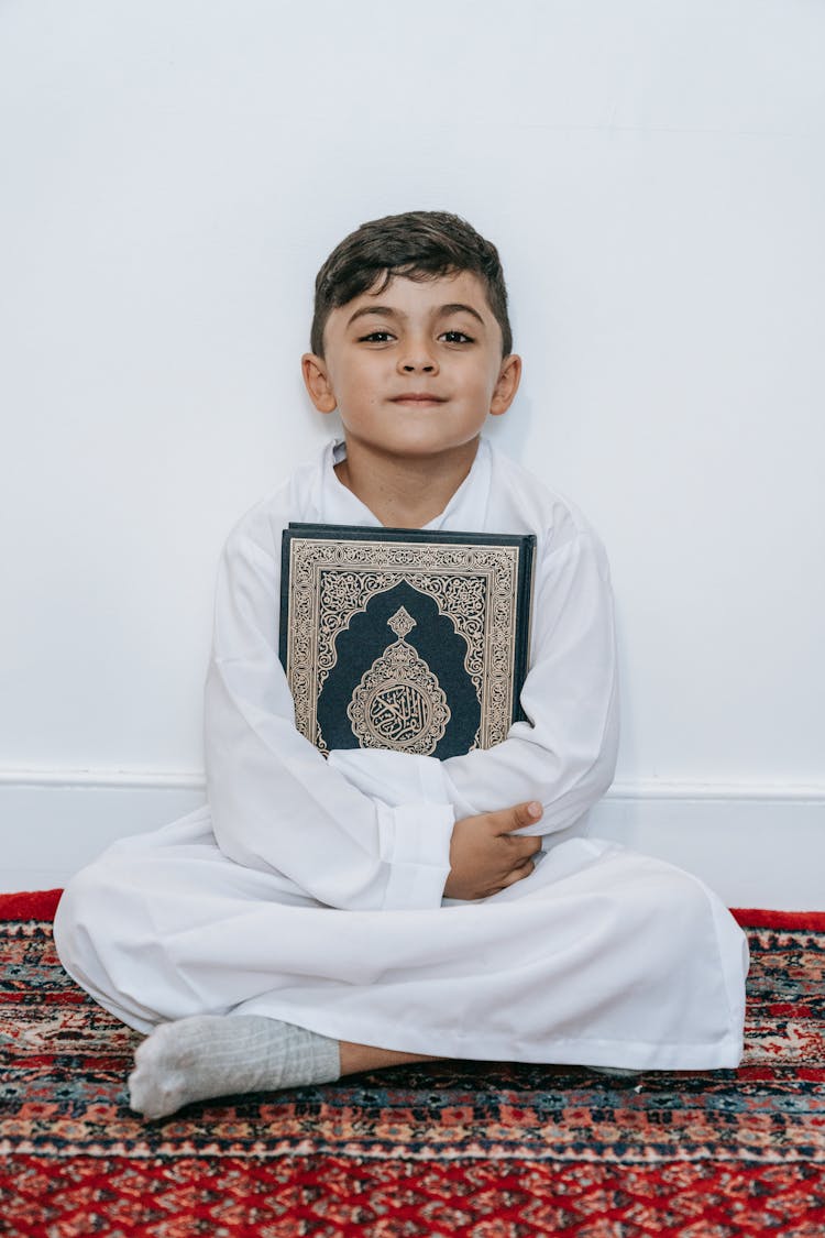 Brunette Boy Sitting Crossed Leg And Holding Koran 