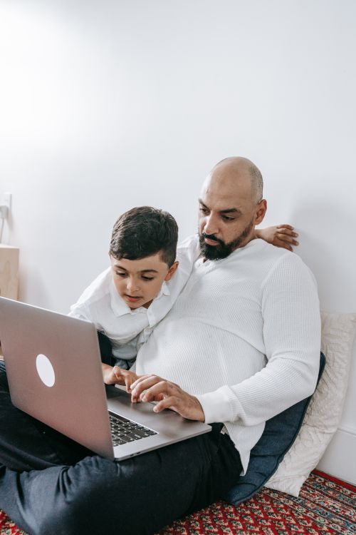 Free Father and son sitting indoors interacting while using a laptop. A heartwarming family moment. Stock Photo