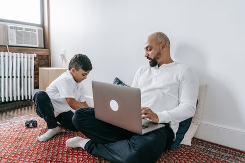 Free Father and son spending quality time together using a laptop at home. Perfect for family and tech themes. Stock Photo