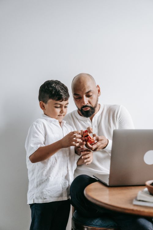 Free A father and son play together with toys beside a laptop in a cozy indoor setting. Stock Photo