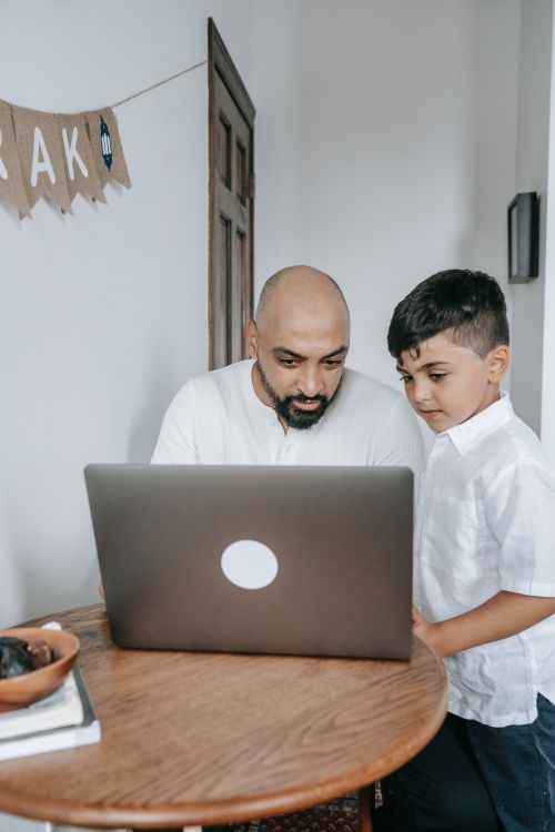 Free Father and son at a table engaged with a laptop, highlighting family connection and technology. Stock Photo