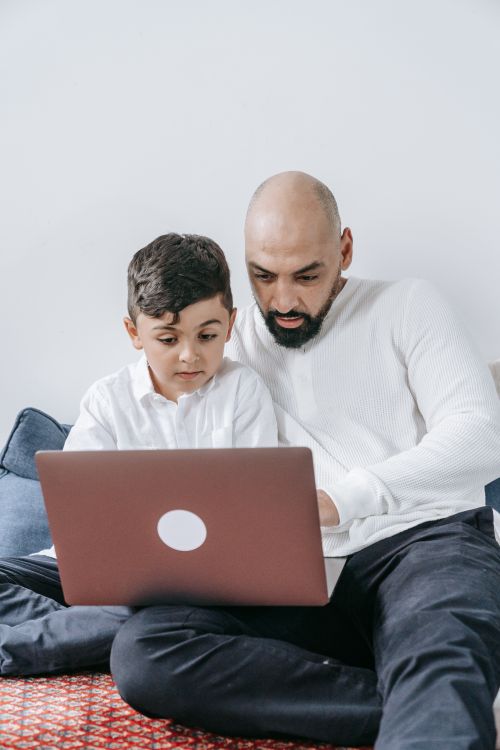 Free Father and son spending quality time together, using a laptop at home. Stock Photo