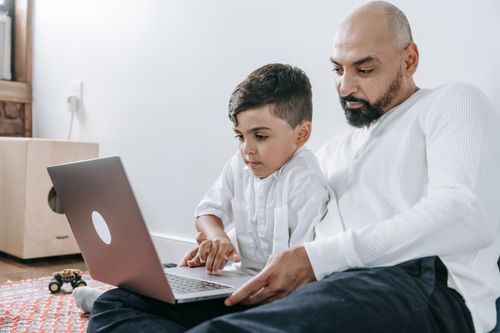 Free A father and son spending quality time together using a laptop, bonding in a cozy indoor setting. Stock Photo
