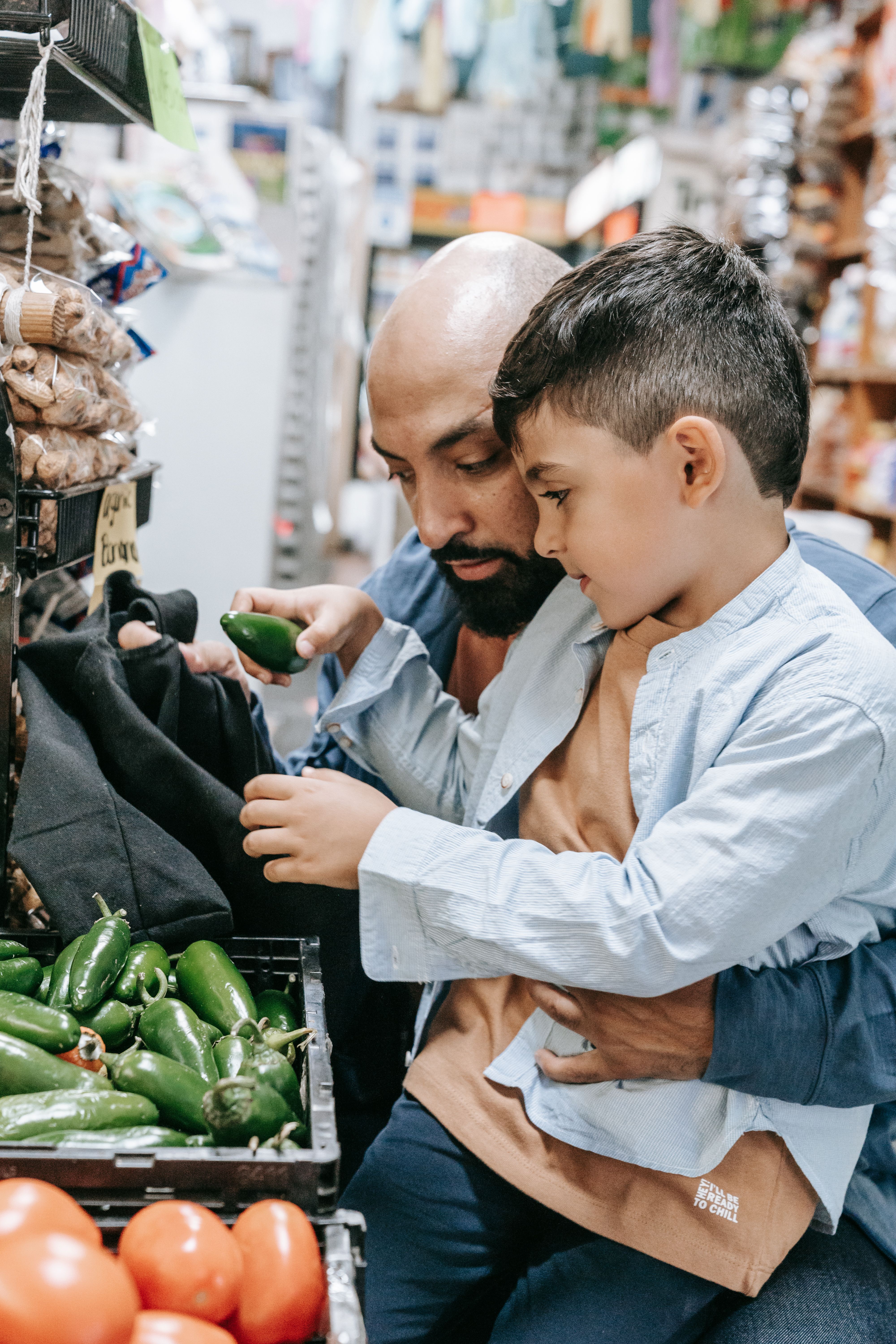 Father and son selecting fresh green bell peppers at a local market, bonding over grocery shopping.