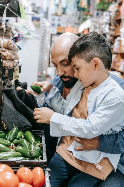 Father and son selecting fresh green bell peppers at a local market, bonding over grocery shopping. Father and son selecting fresh green bell peppers at a local market, bonding over grocery shopping.