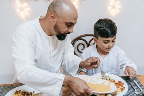 Free Father and son enjoying a home-cooked meal together indoors, sharing quality family time. Stock Photo