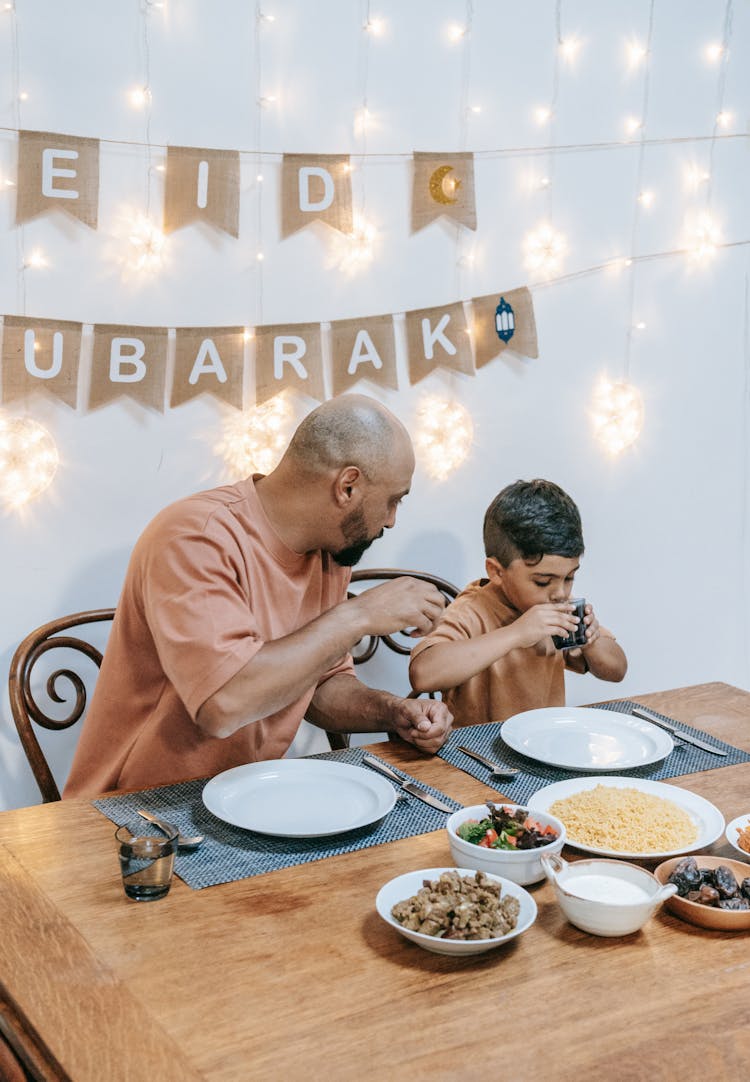 Father And Son Sitting At Table Eating 