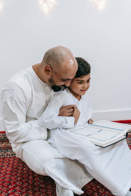 Free Father and son sharing a bonding moment while reading together in traditional attire. Stock Photo