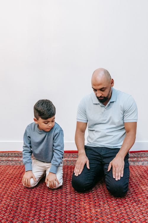 Free A father and son kneel in prayer on a patterned red carpet indoors. Stock Photo