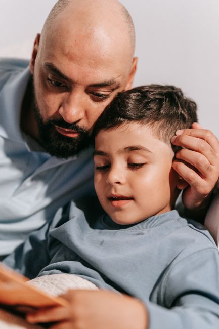 A father and young son bonding while reading together indoors.