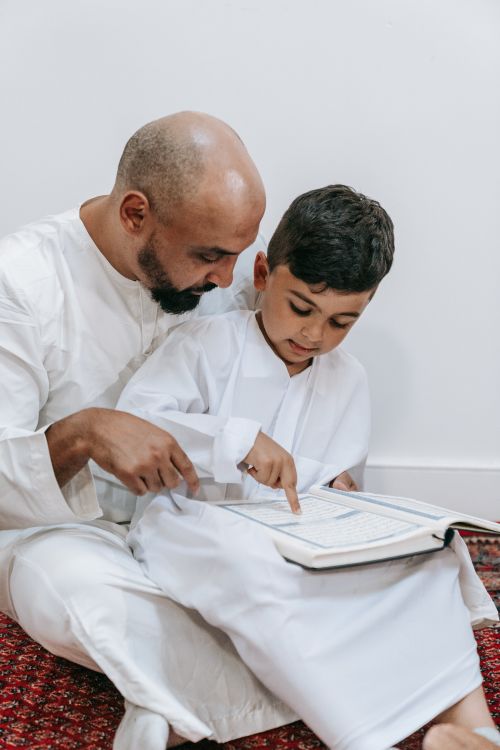 Free A father and son in white traditional attire reading a book together at home. Family bonding moment captured indoors. Stock Photo