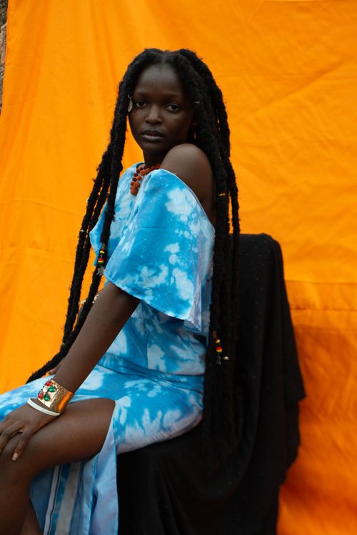 Free Portrait of a woman in blue tie-dye attire with vibrant orange backdrop, embodying African fashion. Stock Photo