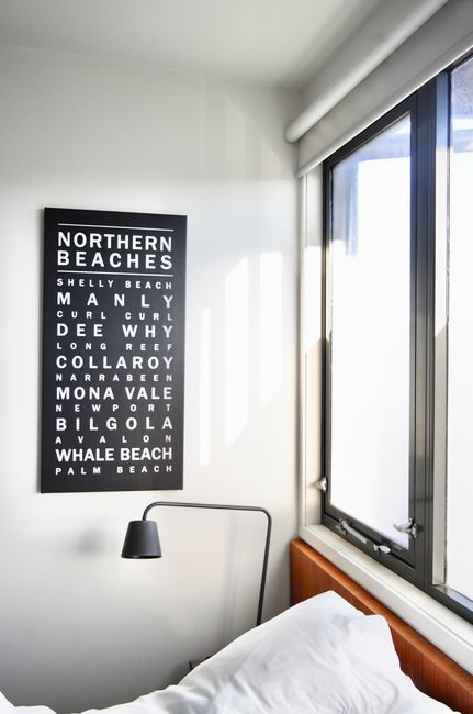 Black and white Northern Beaches typographic wall art poster in minimalist white bedroom with window and reading lamp