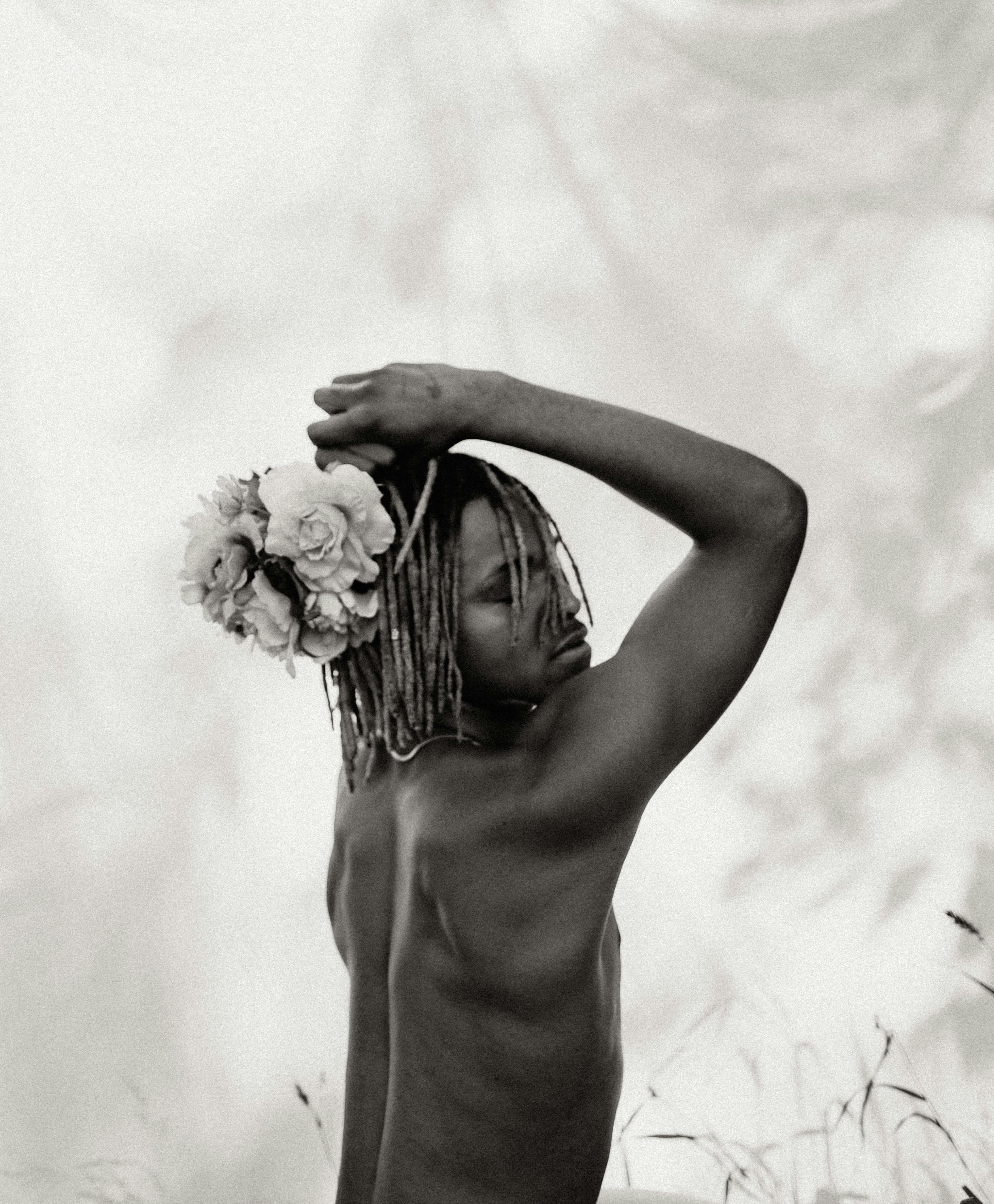 Black and white portrait of a shirtless man with floral headpiece, posing gracefully.
