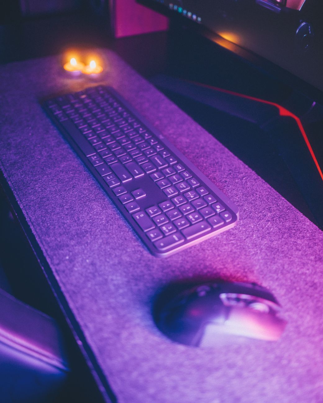 A sleek wireless keyboard and mouse on a modern desk illuminated by neon lighting.
