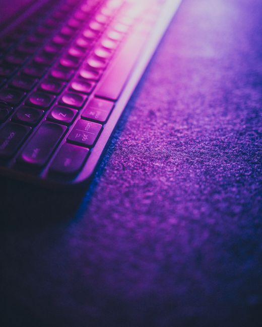 Fotomural Un teclado de ordenador iluminado por vibrantes luces de neón rosas y moradas sobre una superficie texturizada.