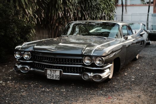Vintage black Cadillac coupe de ville parked on gravel against a leafy backdrop.