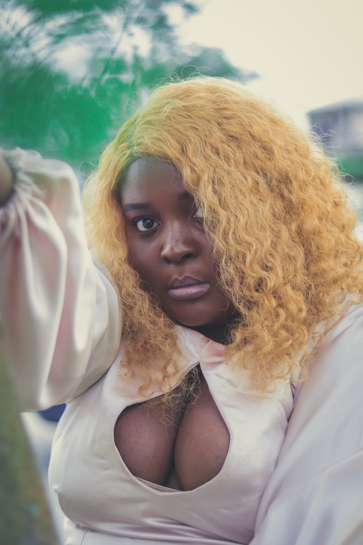 A Woman With Blonde Curly Hair Wearing A Blouse Showing Her Cleavage