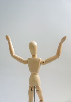 A wooden mannequin with raised arms against a neutral background, symbolizing success and triumph.