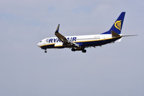 Free Ryanair airplane flying in clear blue sky, showcasing aviation and travel. Stock Photo