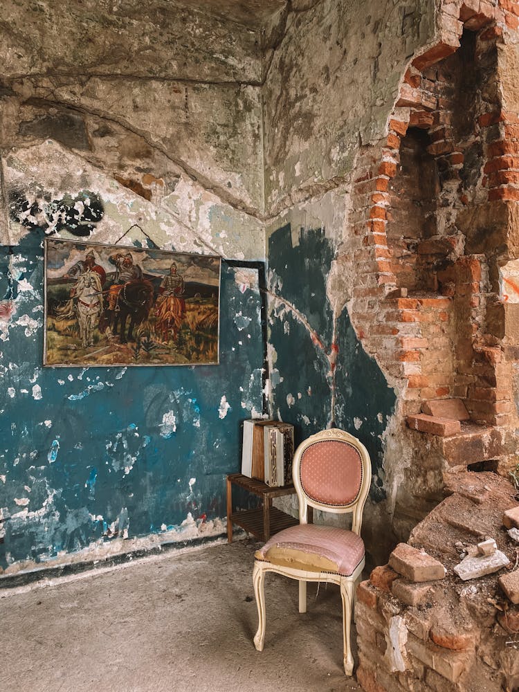 A Wooden Chair And A Painting Hanging On A Shabby Ruined Wall