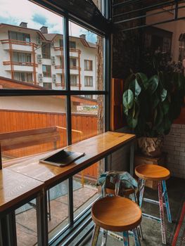 Warm cafe interior in Sochi with wooden tables and stools by a large window.
