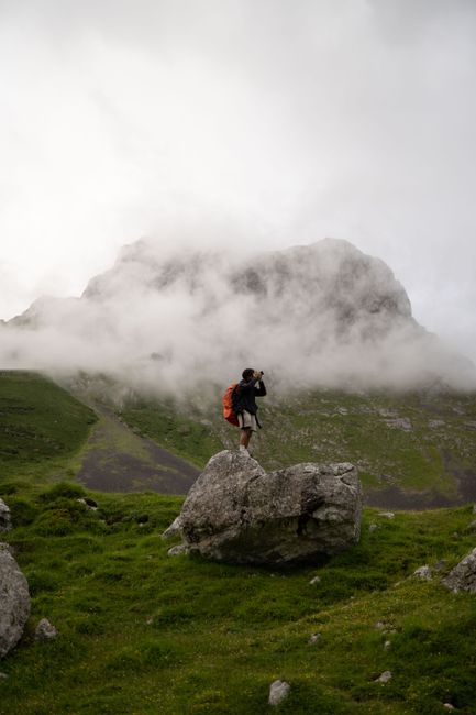 A hiker captures the foggy mountain view standing on a rock.