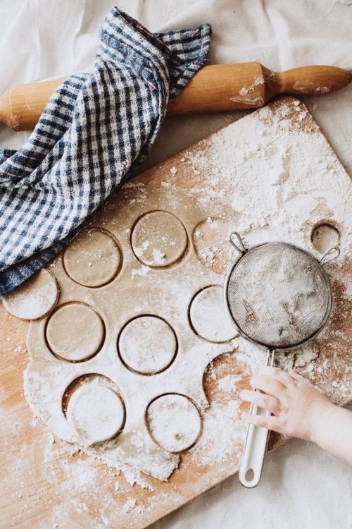 Free Top view of dough preparation with rolling pin, flour, and child's hand touching a sieve. Stock Photo