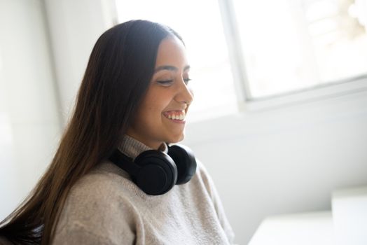 Smiling woman with black headphones and gray sweater enjoying indoors.