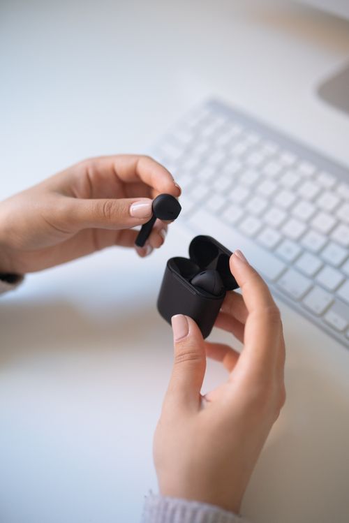 Free Hands holding black wireless earbuds and case near keyboard on a desk. Stock Photo