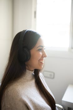 Side view of a woman wearing headphones and smiling indoors by a window.