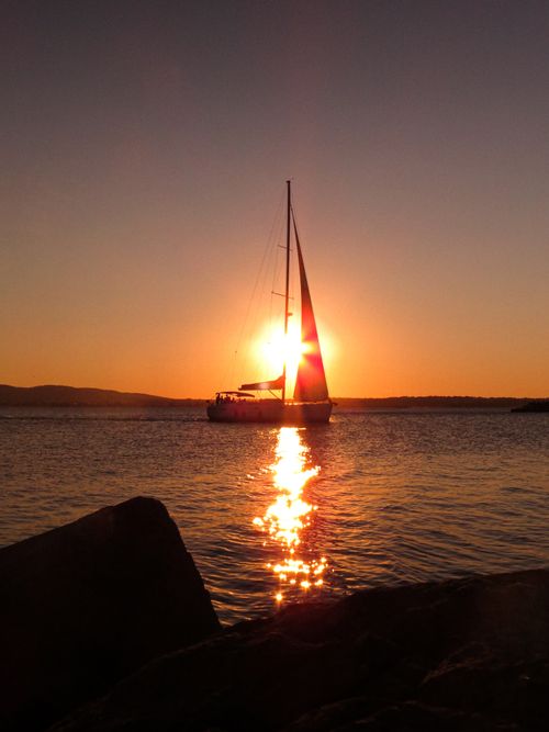 Free A dramatic sailboat silhouette against a golden sunset over calm ocean waters. Stock Photo