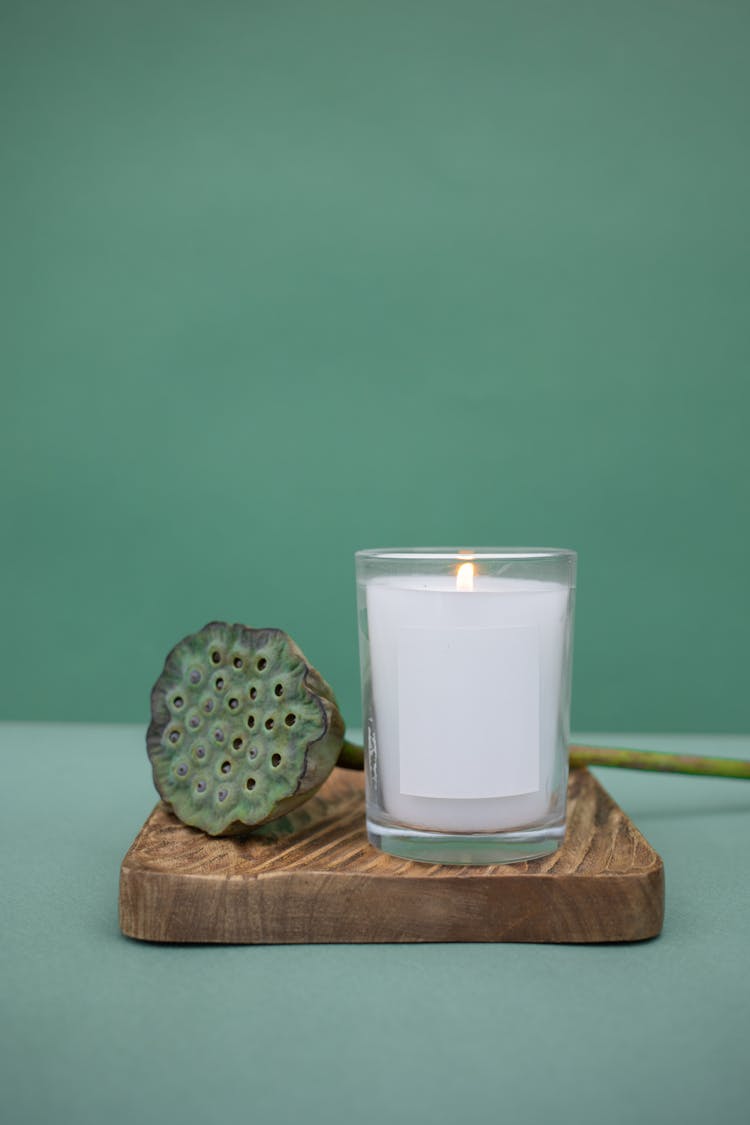 A White Pillar Candle In Clear Glass On A Wooden Board