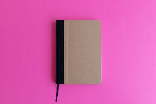 Free Brown notebook with black spine on vibrant pink surface, perfect for mockup designs. Stock Photo