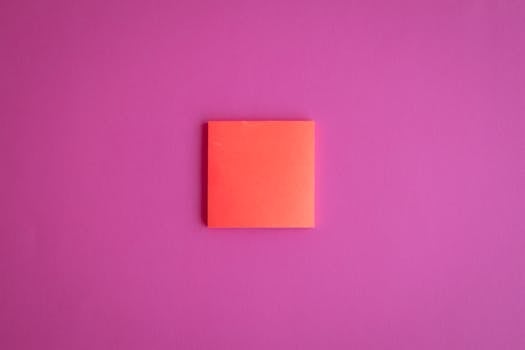 A simple orange sticky note placed on a vibrant pink background, perfect for design concepts.