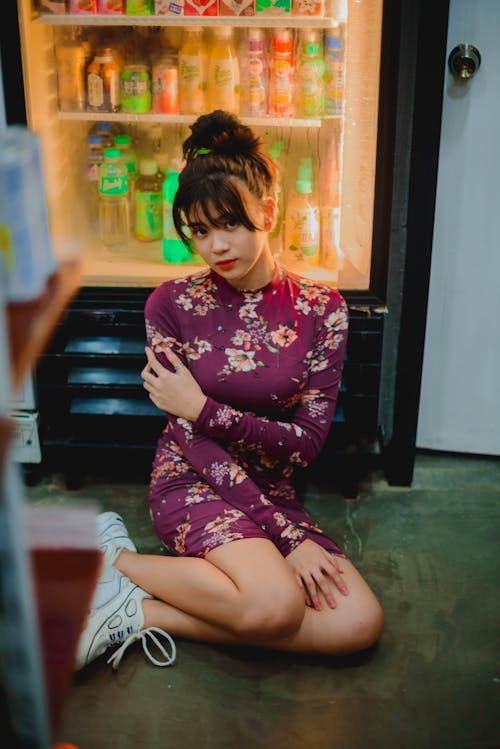Young Asian Woman Sitting next to a Fridge with Cold Drinks