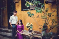 一对夫妇在乡村环境中微笑着，旁边摆着盆栽和竹桌