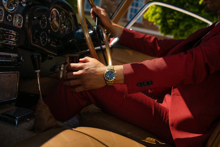 A Person In Red Formal Attire Holding The Gold Steering Wheel Of A Car