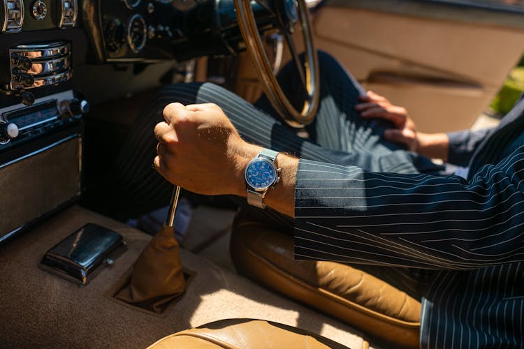 A Man In Formal Attire Wearing Silver Wristwatch While Holding The Shifter Of A Car