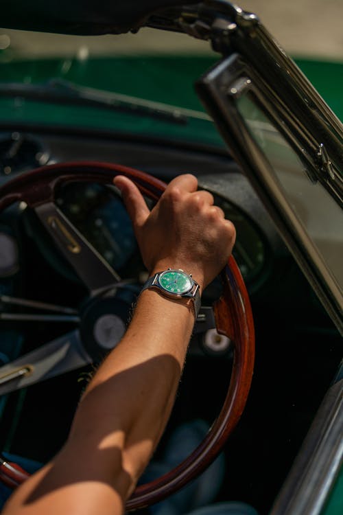 A Person Wearing Silver Wristwatch while Holding the Steering Wheel of a Green Car