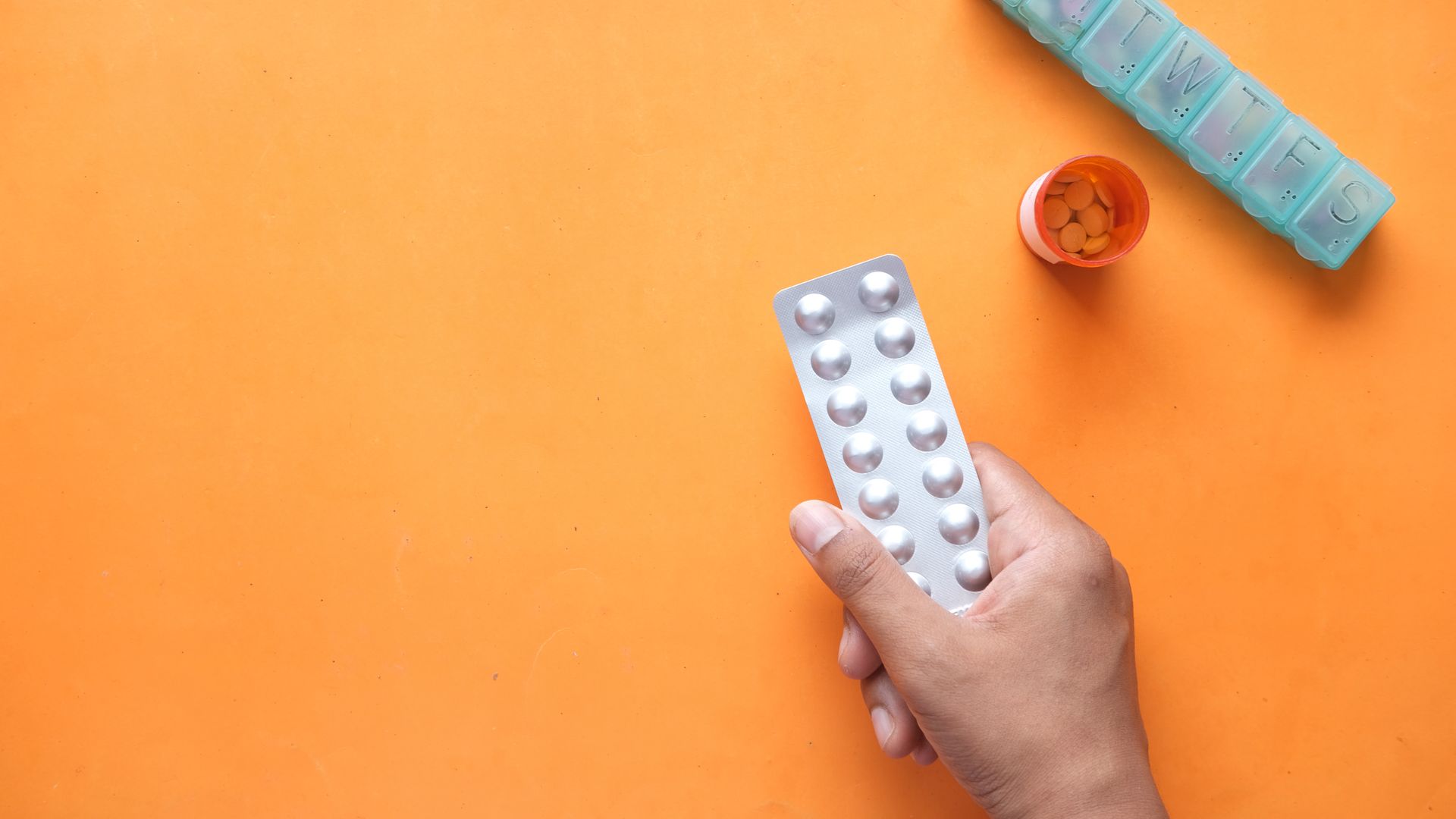 Waklert Review: Boost Your Energy and Focus A hand holding a medicine blister near a pill organizer and orange pill bottle.