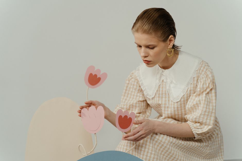 A woman in a checkered dress adds delicate paper flowers in a minimalist setting.
