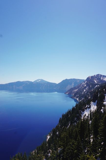 Breathtaking view of Crater Lake, Oregon with clear skies and snow-capped hills.