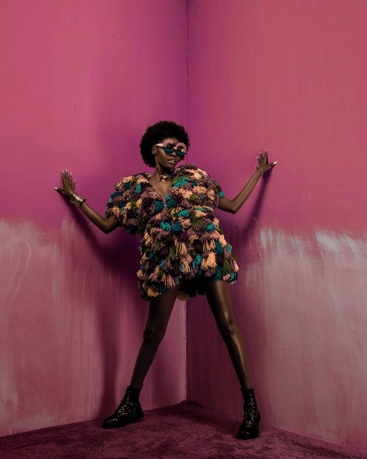 Woman In Colorful Fringe Dress Posing Beside A Pink Wall