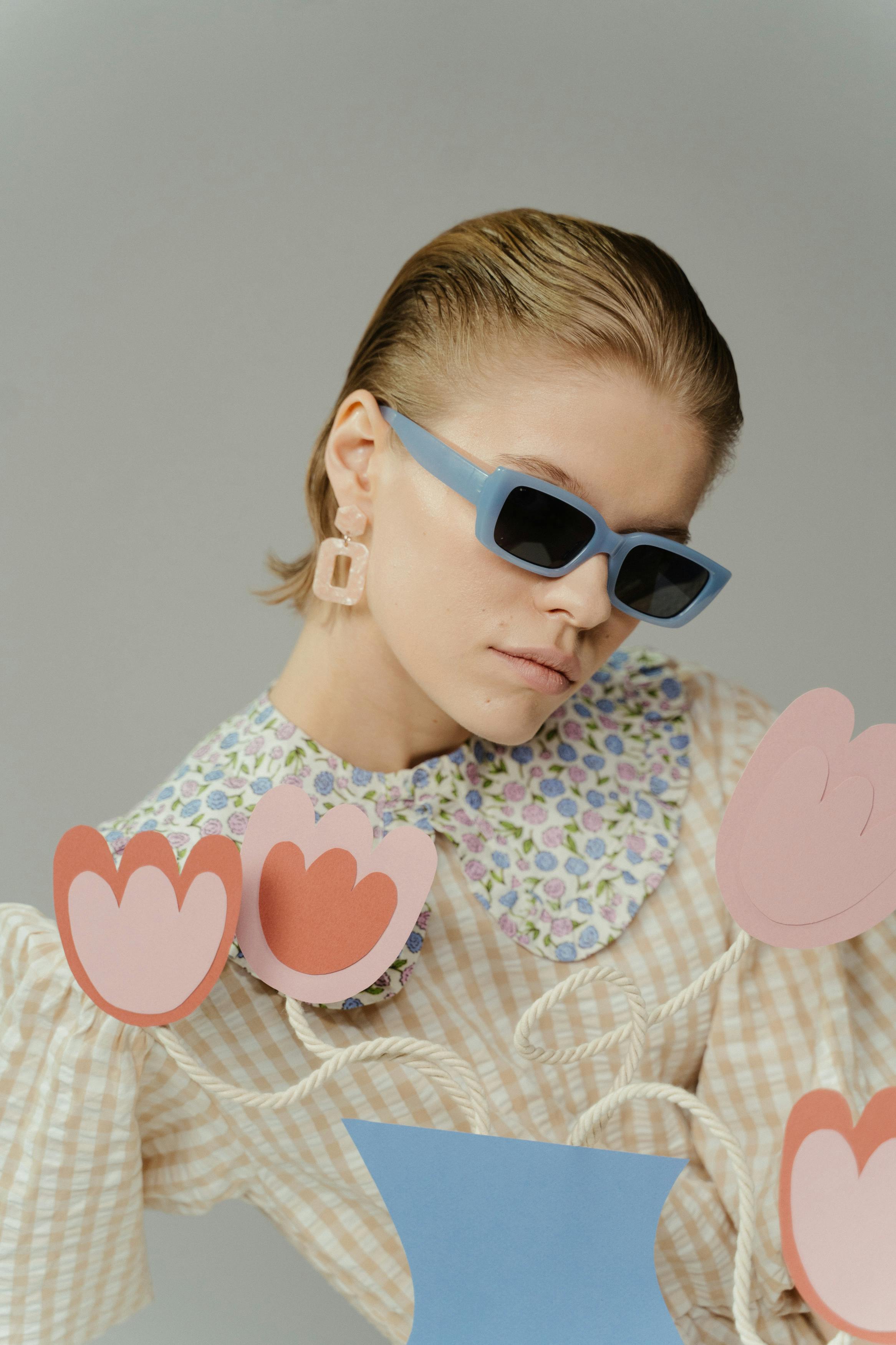 Stylish woman wearing sunglasses and floral shirt posing with paper tulip accents.