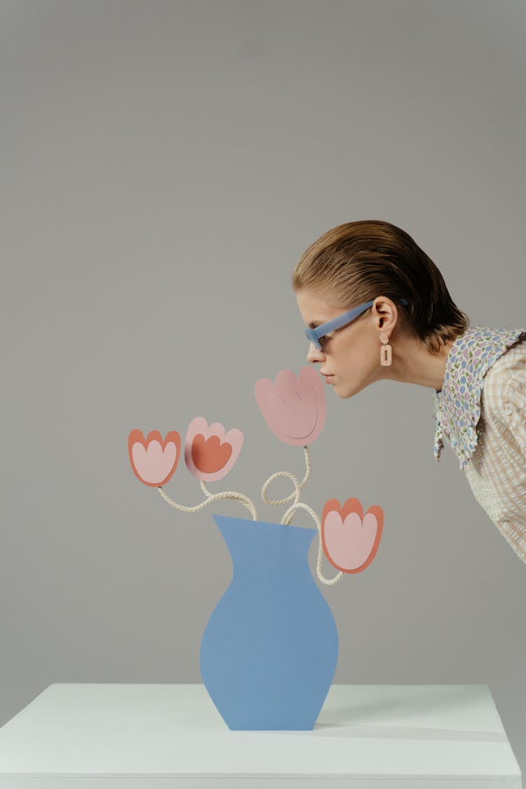 A Woman In A Stage Play Smelling Flowers Made Of Paper Cut Outs In Blue Vase