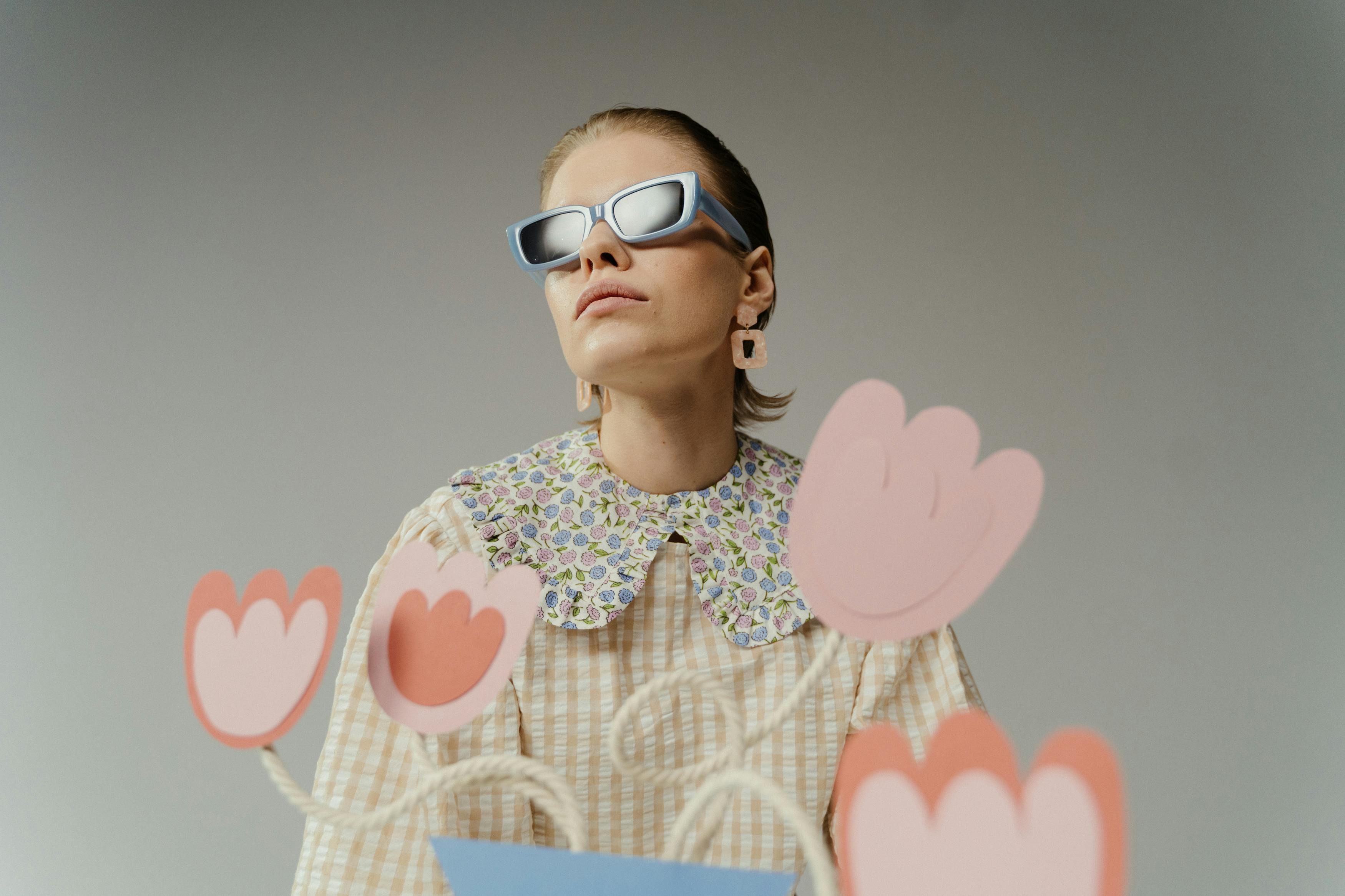Fashionable woman in sunglasses with creative cardboard flowers indoors.