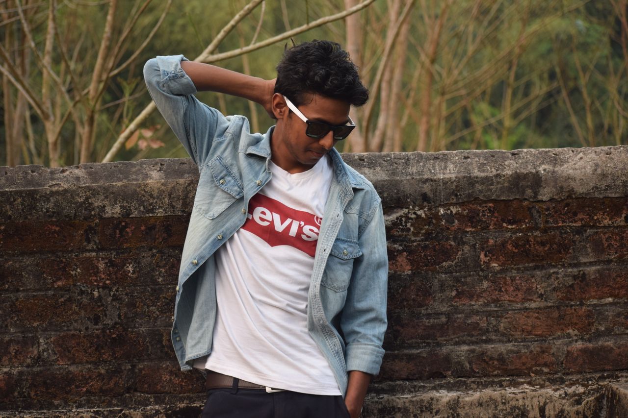 young man posing in denim jacket and sunglasses exuding style and conf