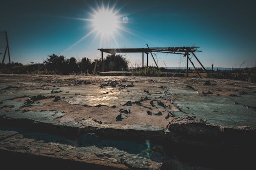 A rustic landscape features a weathered wooden shed under the bright sun with sunrays casting dramatic shadows.